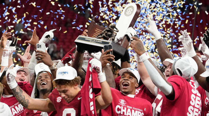 Alabama football players celebrate winning the 2023 SEC championship over Georgia by hoisting a trophy.
